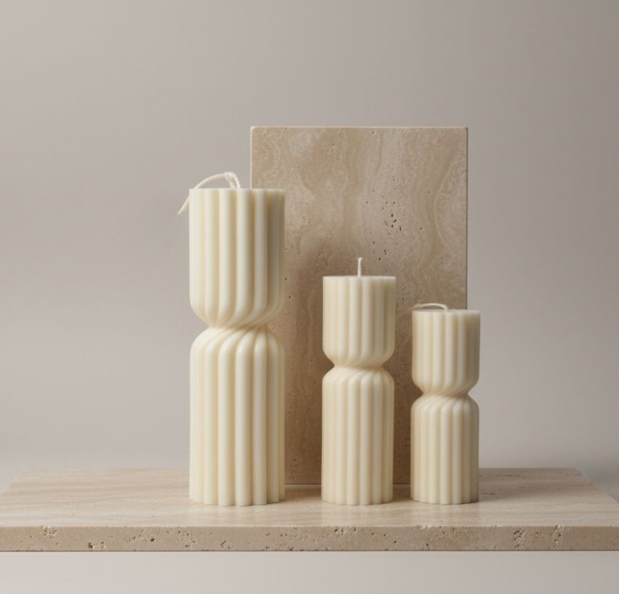 Trzy świece dekoracyjne Pillar marki Candelovo w różnych rozmiarach, ustawione na beżowym tle z kamienną podstawą